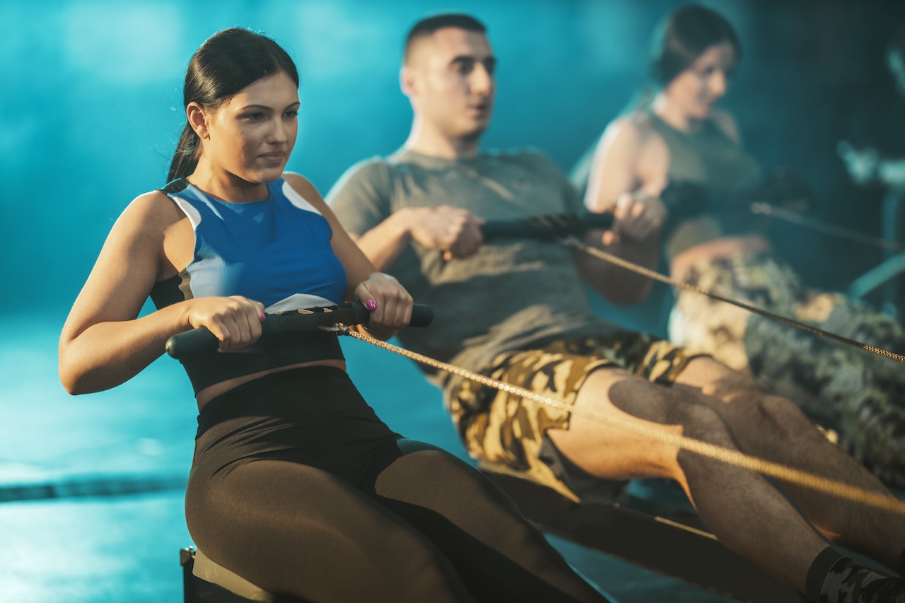 CrossFit for beginners: woman and men performing rowing exercise during a workout session.