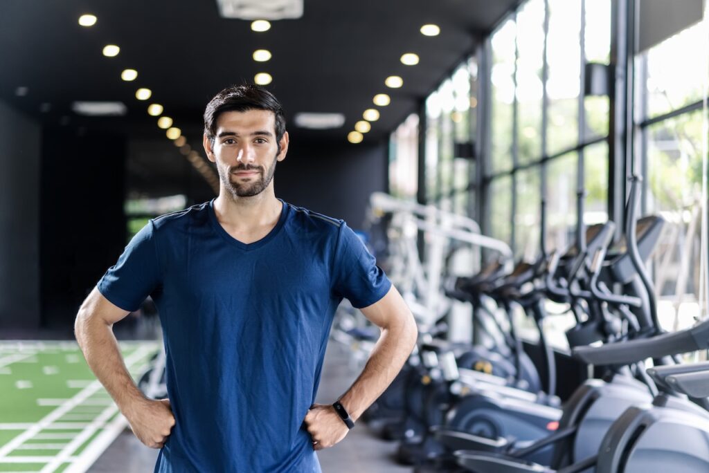 Man in blue shirt confidently standing in a modern gym, highlighting the concept of overcoming fitness plateaus