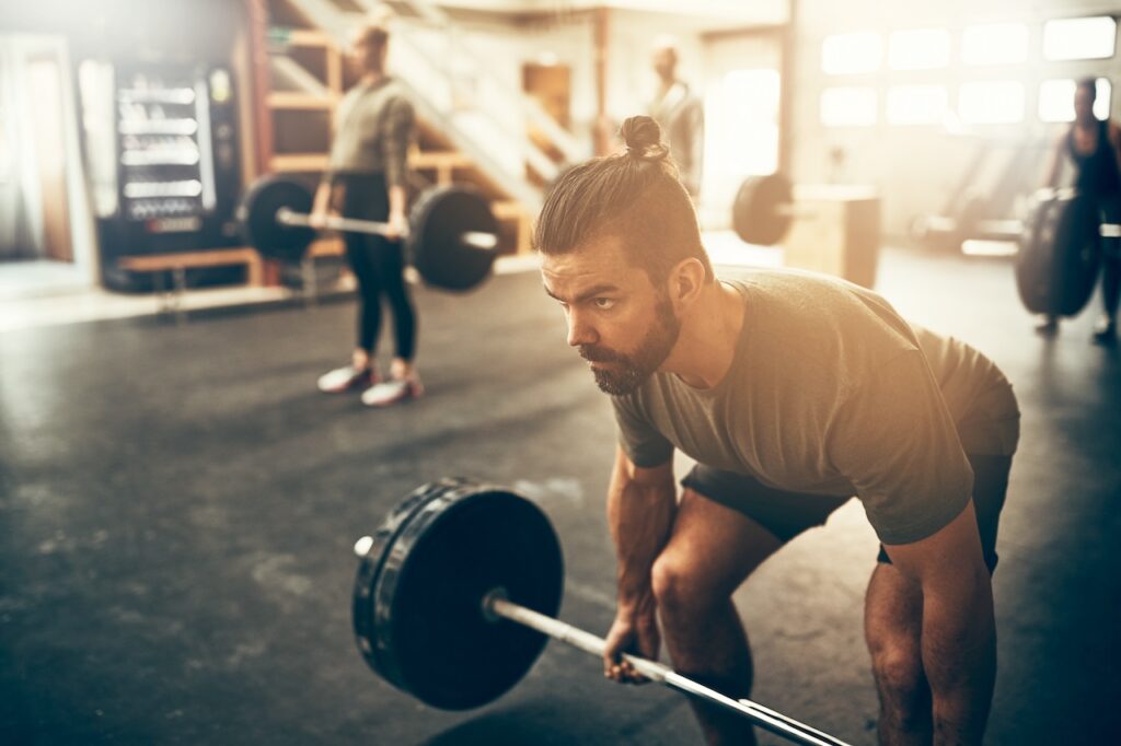 Man in his prime, staying fit over 50, lifting a barbell with determination in a sunlit gym.