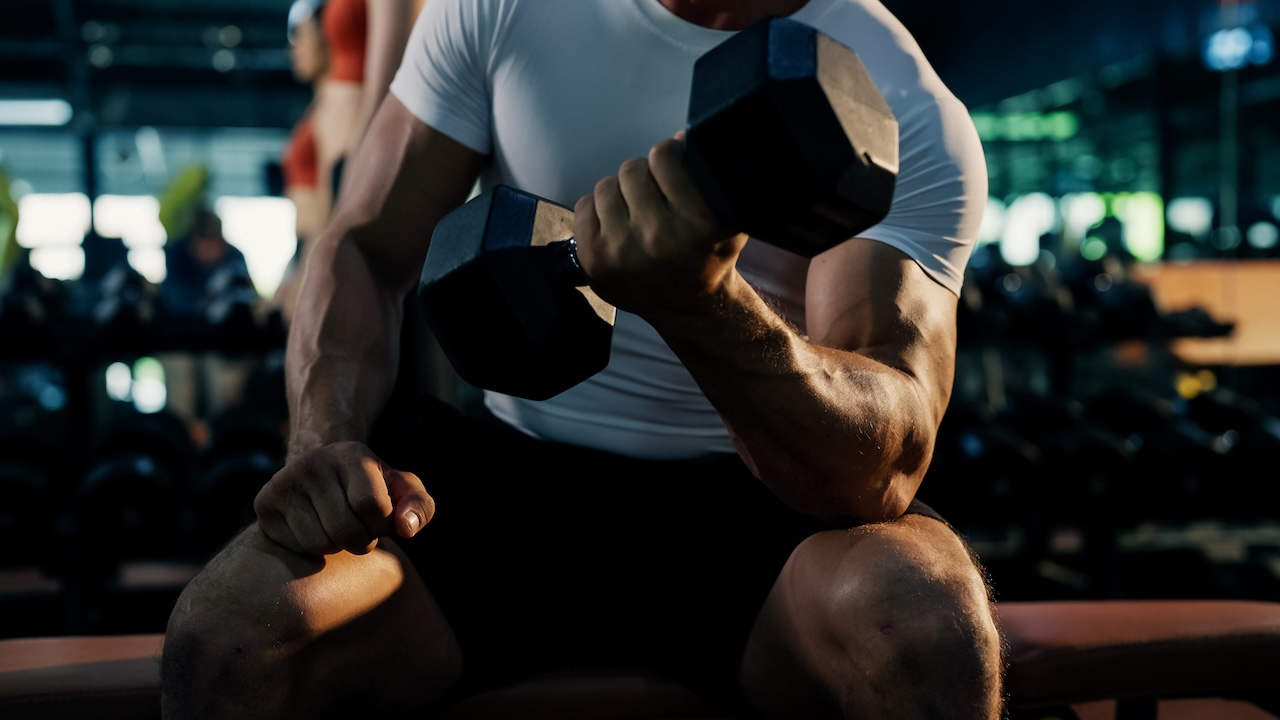 An individual performing a dumbbell curl in a gym setting, illustrating a technique used in intermediate strength training routines.