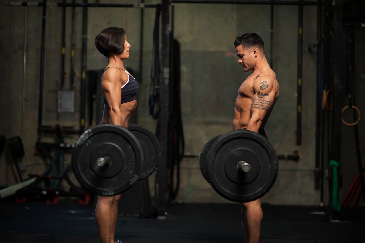 Two athletes practicing advanced lifting techniques with barbells in a gym, focusing on form and strength training.
