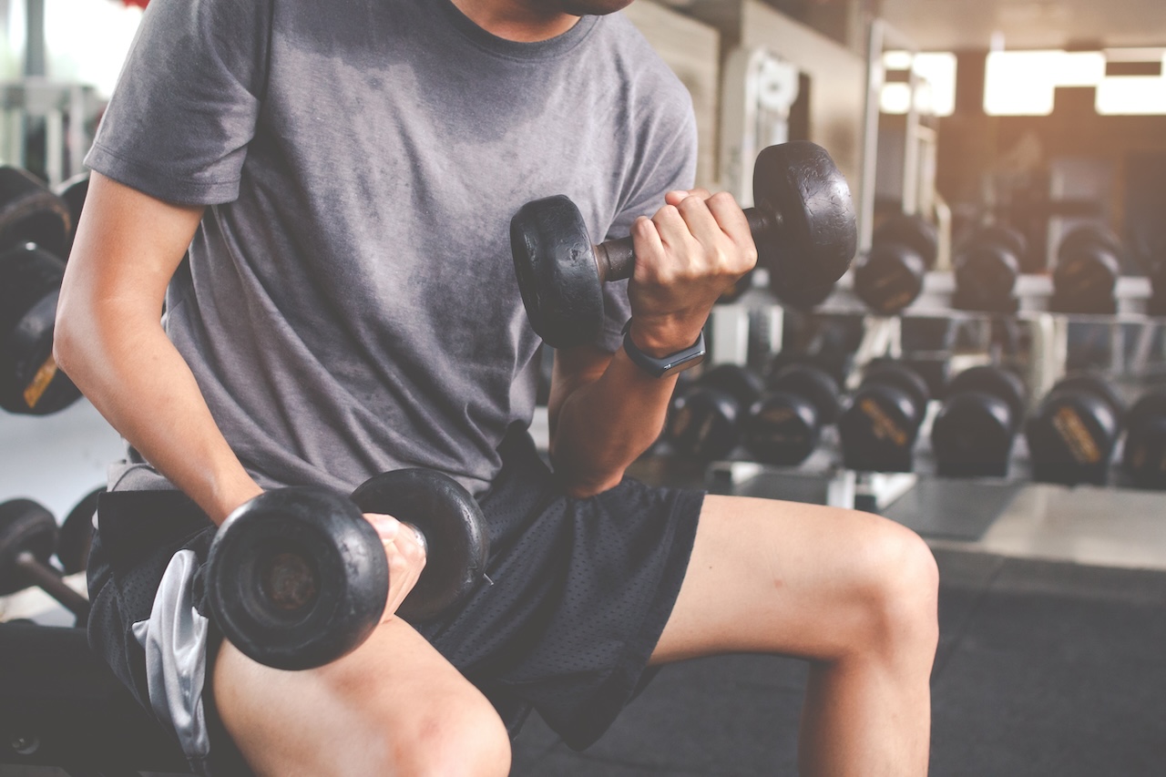 A man in a gym performing a bicep curl with a dumbbell, illustrating a beginning strength training exercise.