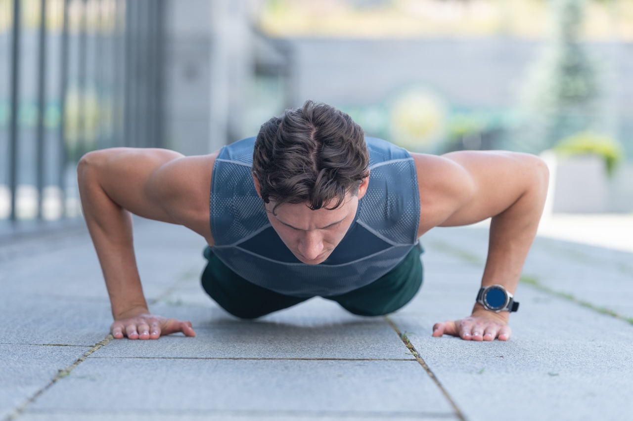 A man in sportswear doing a push-up outdoors, demonstrating bodyweight training for strength.