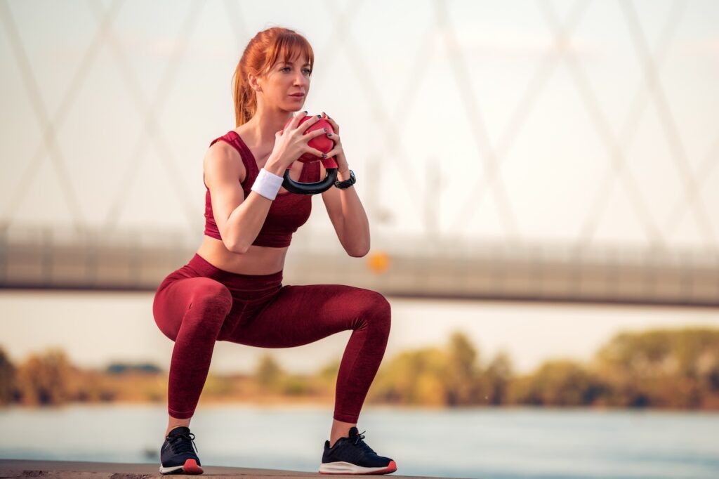 A woman performing a squat exercise with a kettlebell to strengthen her core, demonstrating a more dynamic and functional movement than traditional sit-ups.
