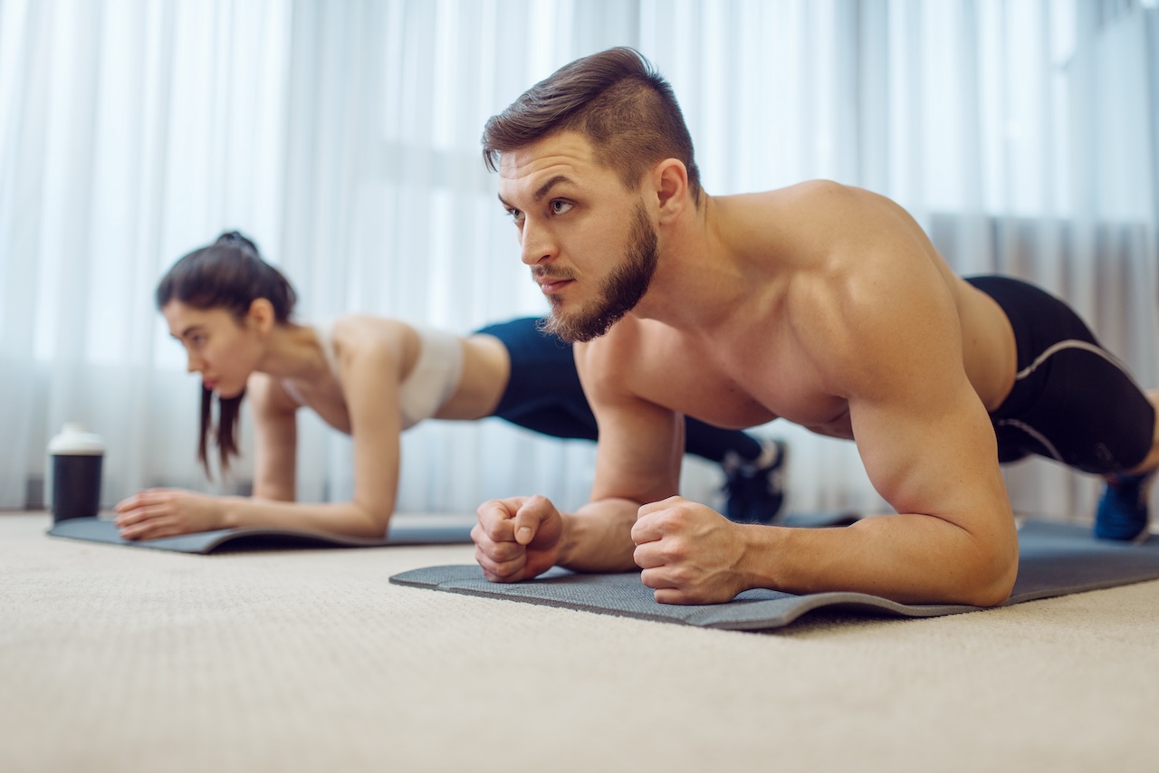 A man and a woman performing a plank exercise on yoga mats, showcasing strength training at home.