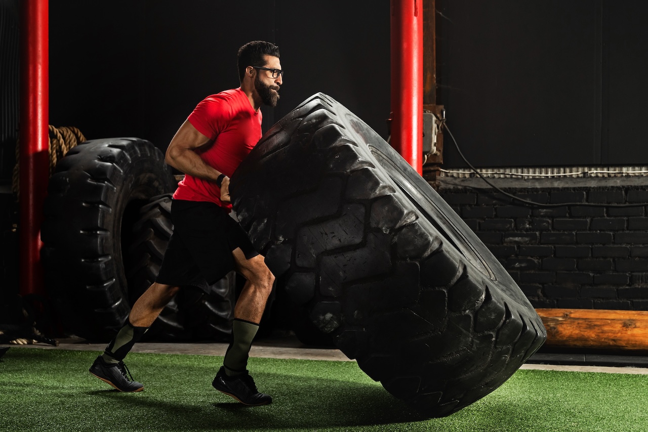 A man performing a functional strength training exercise by flipping a large tire in a gym.