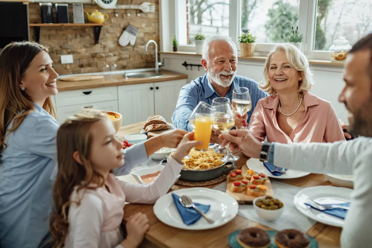 A multi-generational family enjoying a meal together, toasting with glasses of wine and orange juice at a dining table filled with various dishes, depicting a scene that brings to mind the consideration of "how many calories should I eat a day by age".