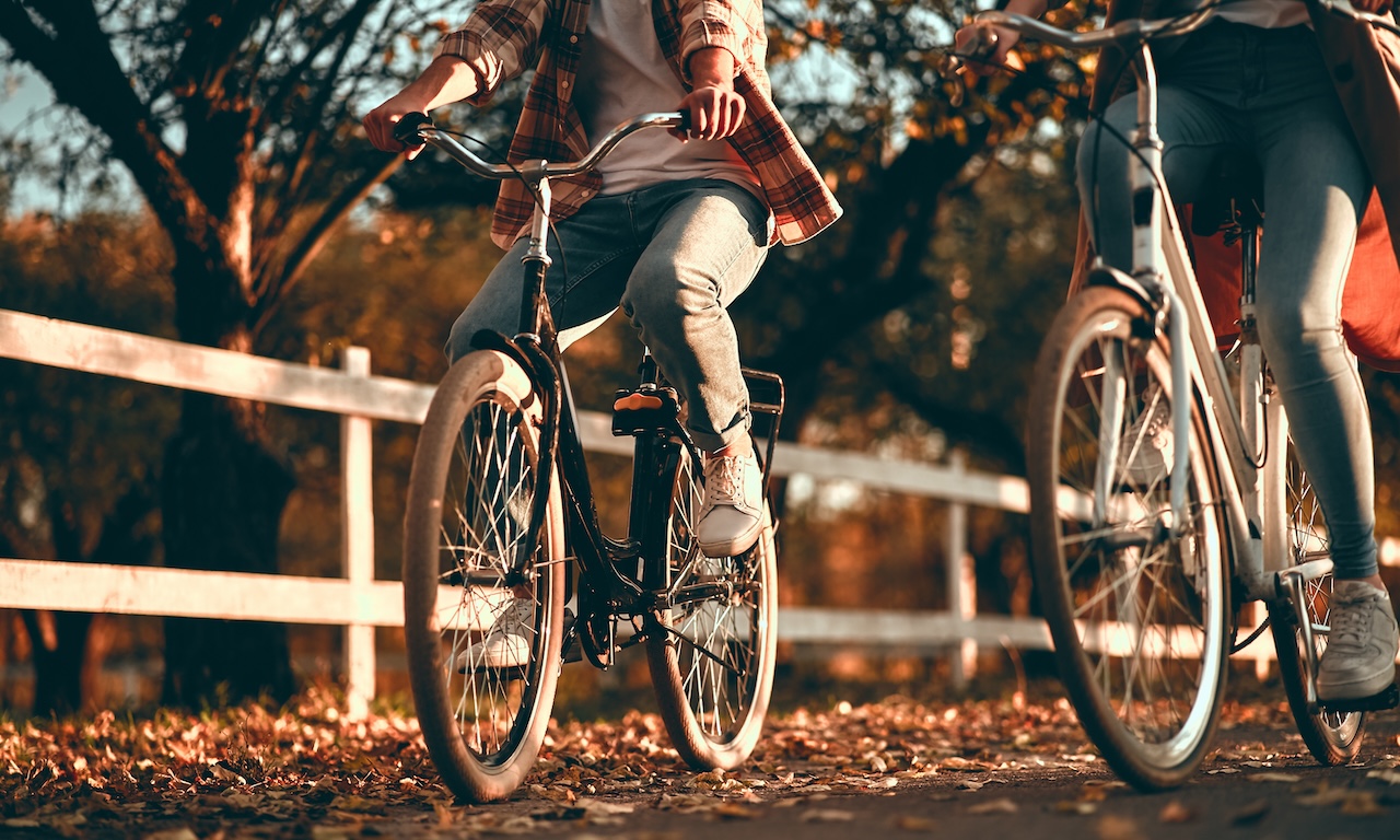 Two people leisurely riding bicycles on a path covered with autumn leaves, suggesting the health benefits and enjoyment of cycling as a form of exercise.