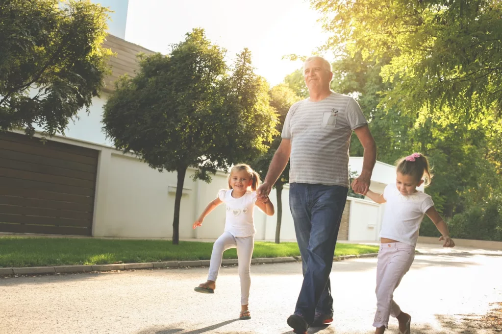 An older gentleman taking a leisurely walk with his two young granddaughters, working on lowering cholesterol by exercise.